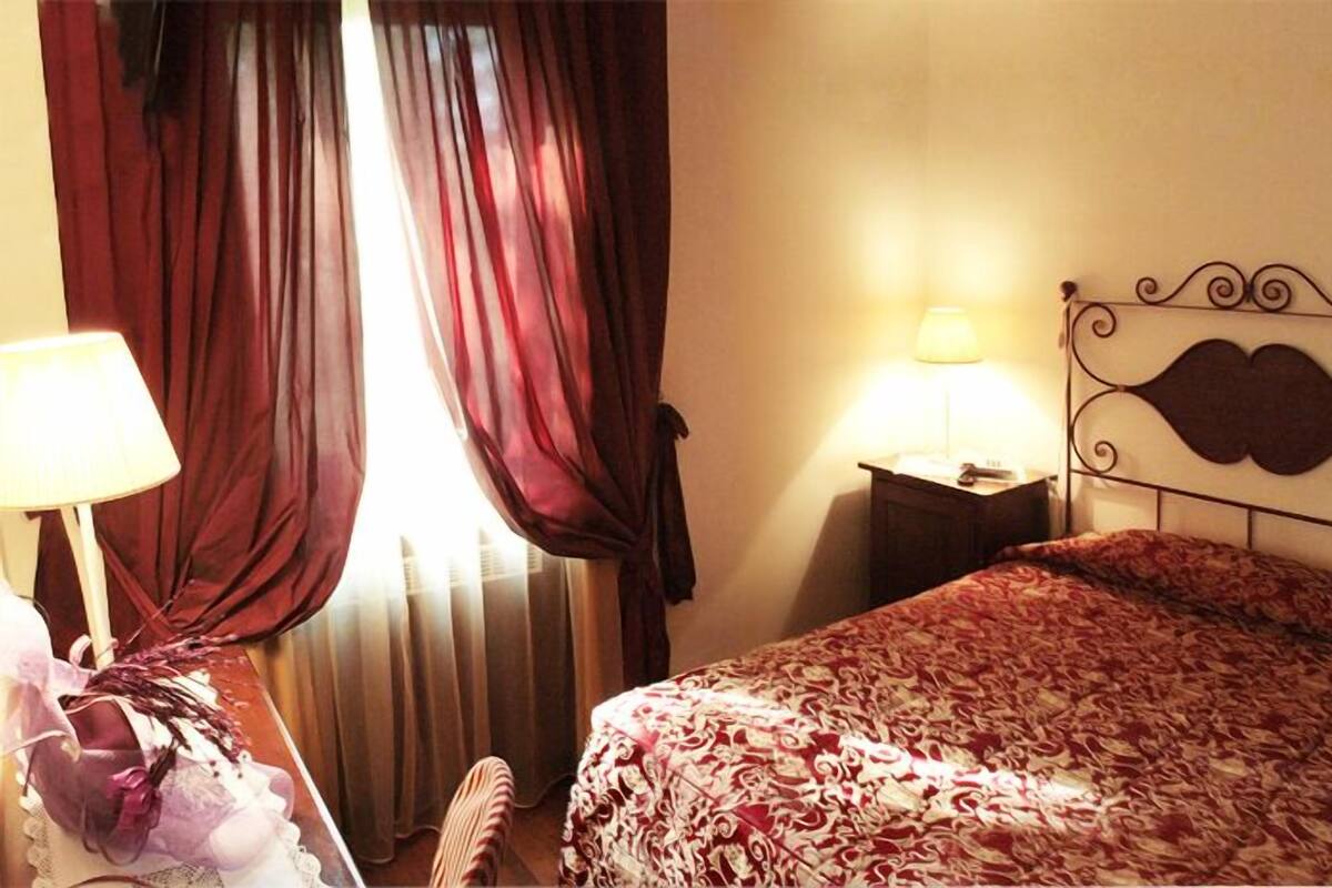 A hotel room with a bed, a nightstand, a lamp, and a window with curtains.
