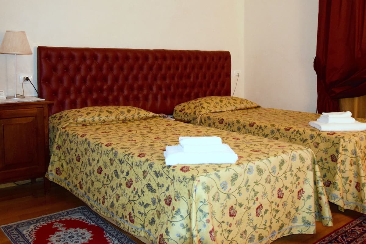 A hotel room with two beds, a nightstand, a lamp, and a red curtain.