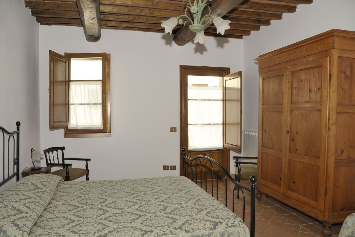 Un dormitorio con una cama, un armario de madera, un escritorio con una silla y dos ventanas con cortinas.