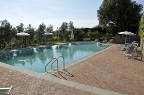 Een buitenzwembad, parasols bij het zwembad en ligstoelen