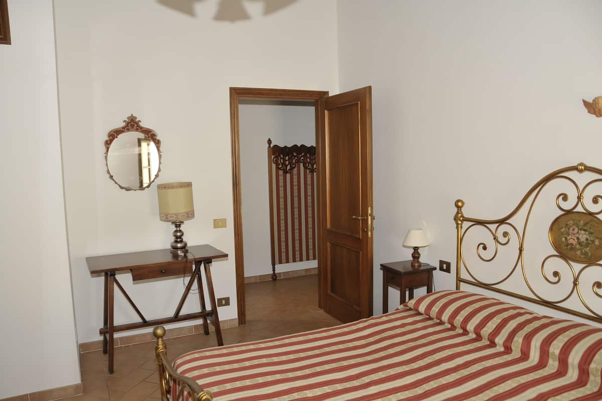 Un dormitorio con cama, escritorio, silla, espejo y puerta que da a otra habitación.