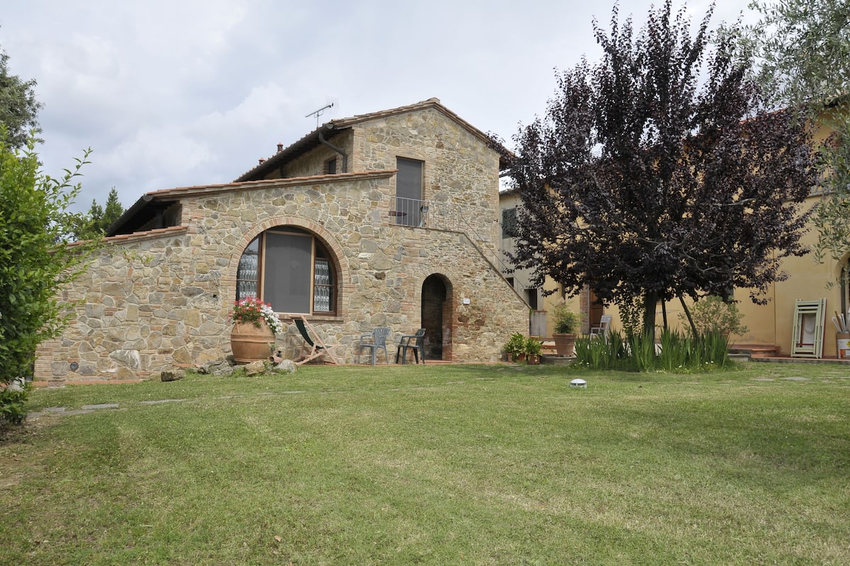 Un edificio de piedra con un gran arco de entrada, un balcón pequeño y un árbol en el patio.