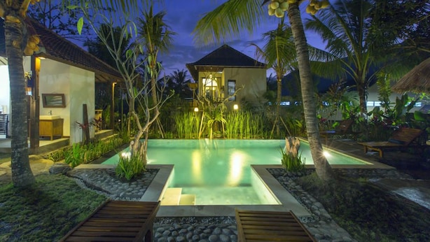 A resort with a swimming pool surrounded by palm trees and tropical plants, a thatched-roof structure, and a well-lit entrance. - Arimba Resort Ubud (Ubud)