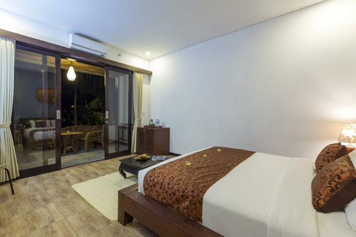 A bedroom with a large bed, a nightstand, a desk, and a sliding glass door leading to an outdoor area with a table and chairs.