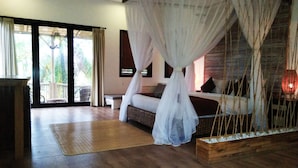 A bedroom with a canopy bed, a wooden floor, a bench, and a view of palm trees. - Arimba Resort Ubud (Ubud)