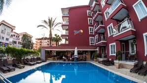 A swimming pool with lounge chairs and a bar area in a hotel with a red facade and balconies. - My Home Apart Hotel (Alanya)