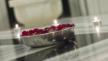 A polished table with a bowl of rose petals and lit candles, reflecting on the surface.