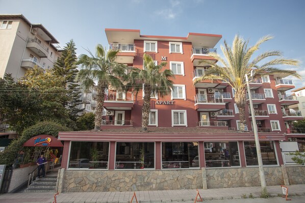 A multi-story hotel with a red facade, balconies, and a restaurant at the ground level. - My Home Apart Hotel (Alanya)