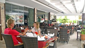 An outdoor dining area with wicker chairs and tables, glass partitions, and a view of the street. - My Home Apart Hotel (Alanya)