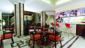 Een hotel lobby met een bar, diverse zithoeken en een trap naar een verdieping.