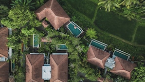 Eine Vogelperspektive zeigt einen luxuriösen Urlaubsort mit mehreren Gebäuden, jedes mit einem markanten, geometrischen Dach, umgeben von üppiger Vegetation und Palmen.
