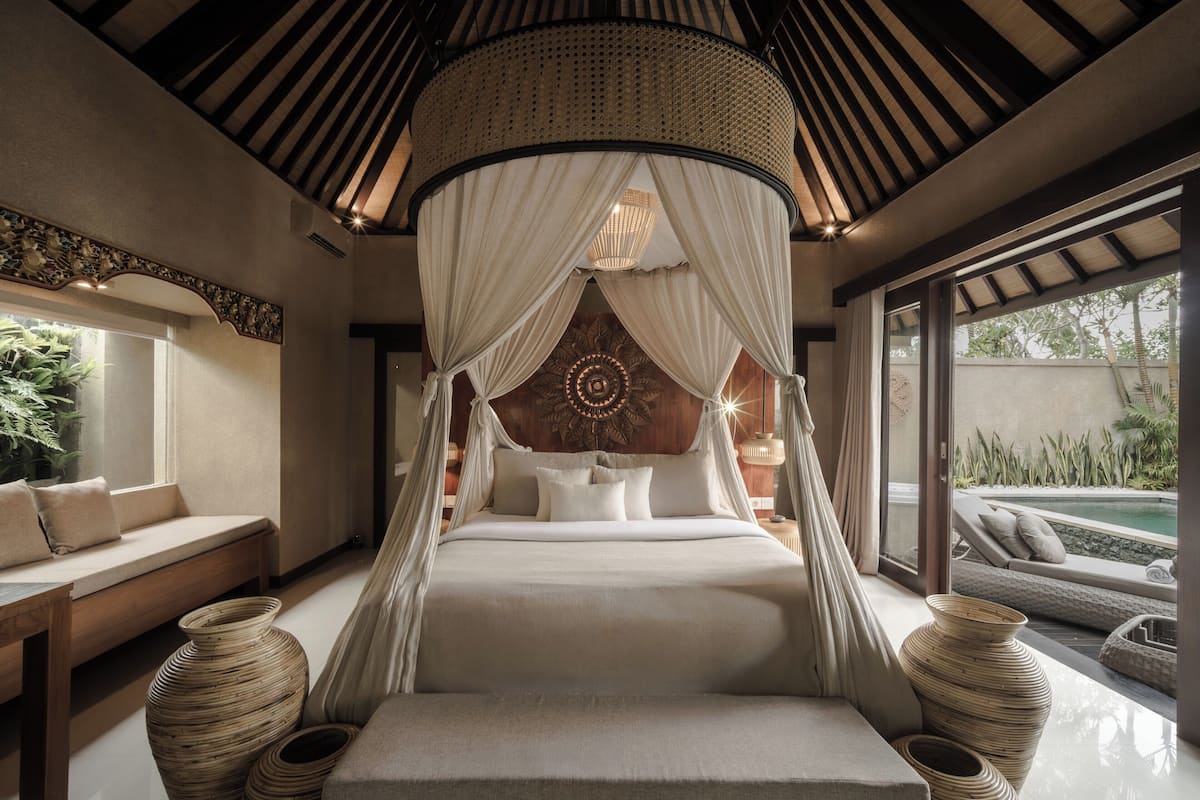 A bed with a canopy, a bench, and a view of the outdoors.