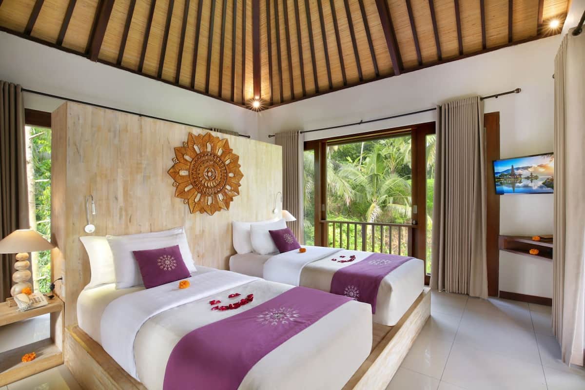 A hotel room with two beds, a decorative wall piece, a television, and a view of greenery.