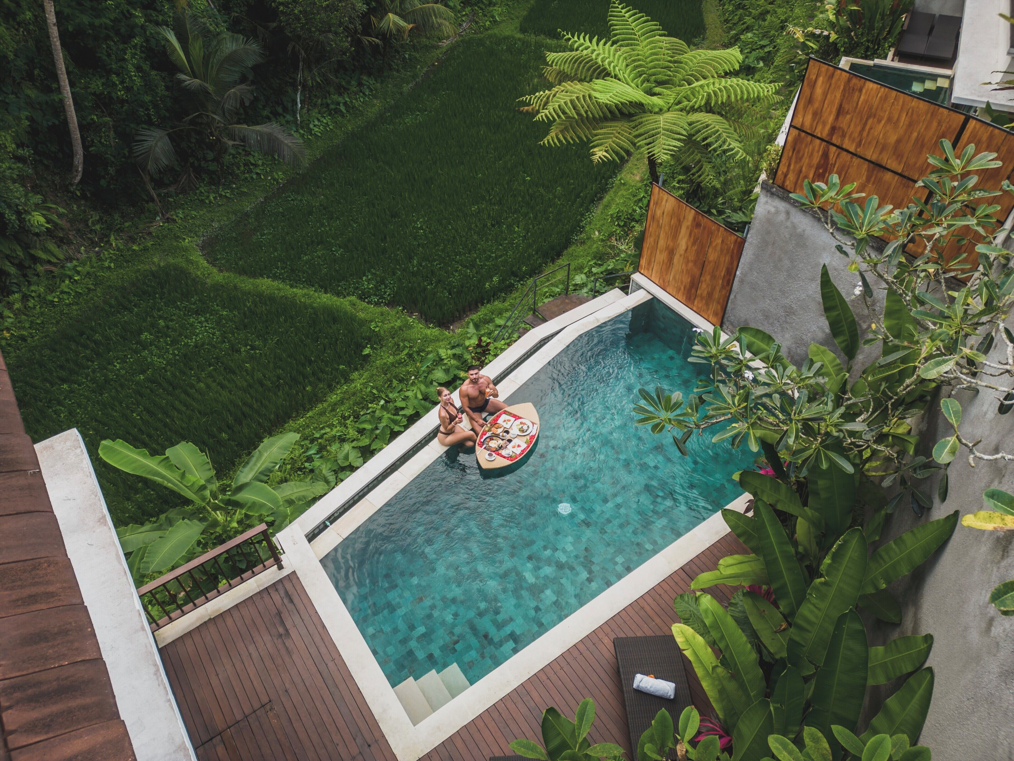 Una piscina con cubierta de madera y abundante vegetación alrededor.