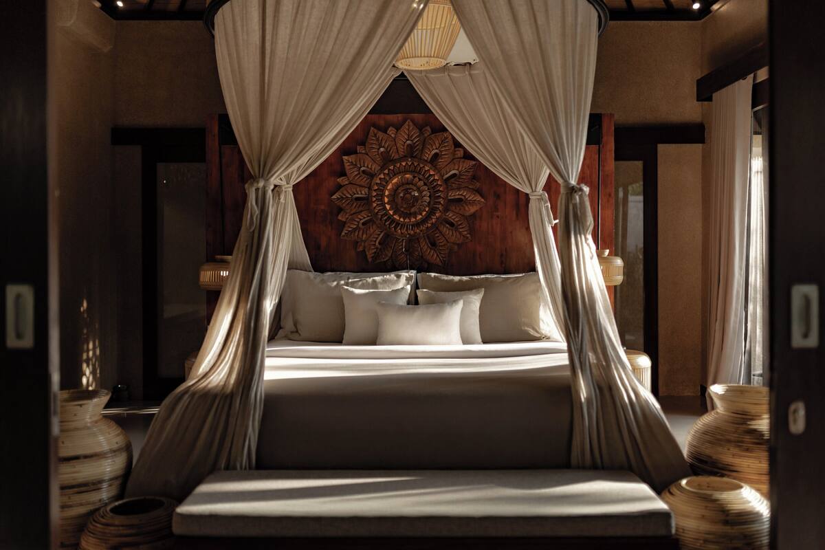 A bedroom with a canopy bed, a decorative wall panel, and a large window.