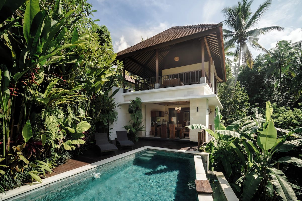 A two-story house with a swimming pool surrounded by lush greenery.