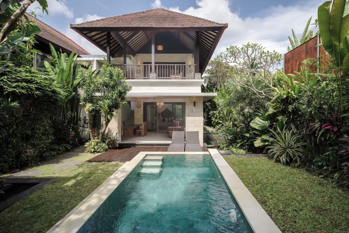 A two-story house with a swimming pool, surrounded by lush greenery.