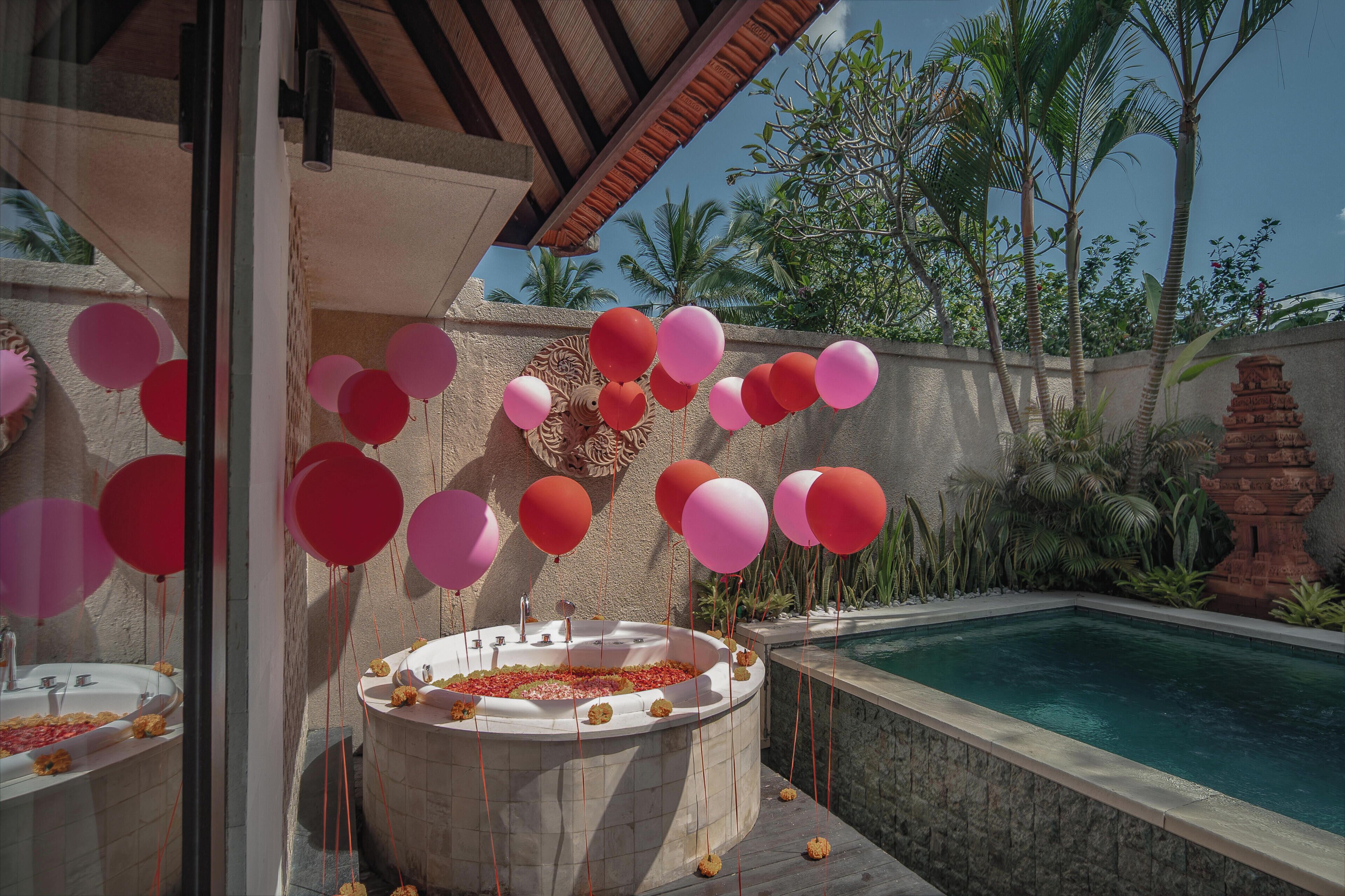 A hot tub with a pool, surrounded by a stone wall, palm trees, and a clear sky.
