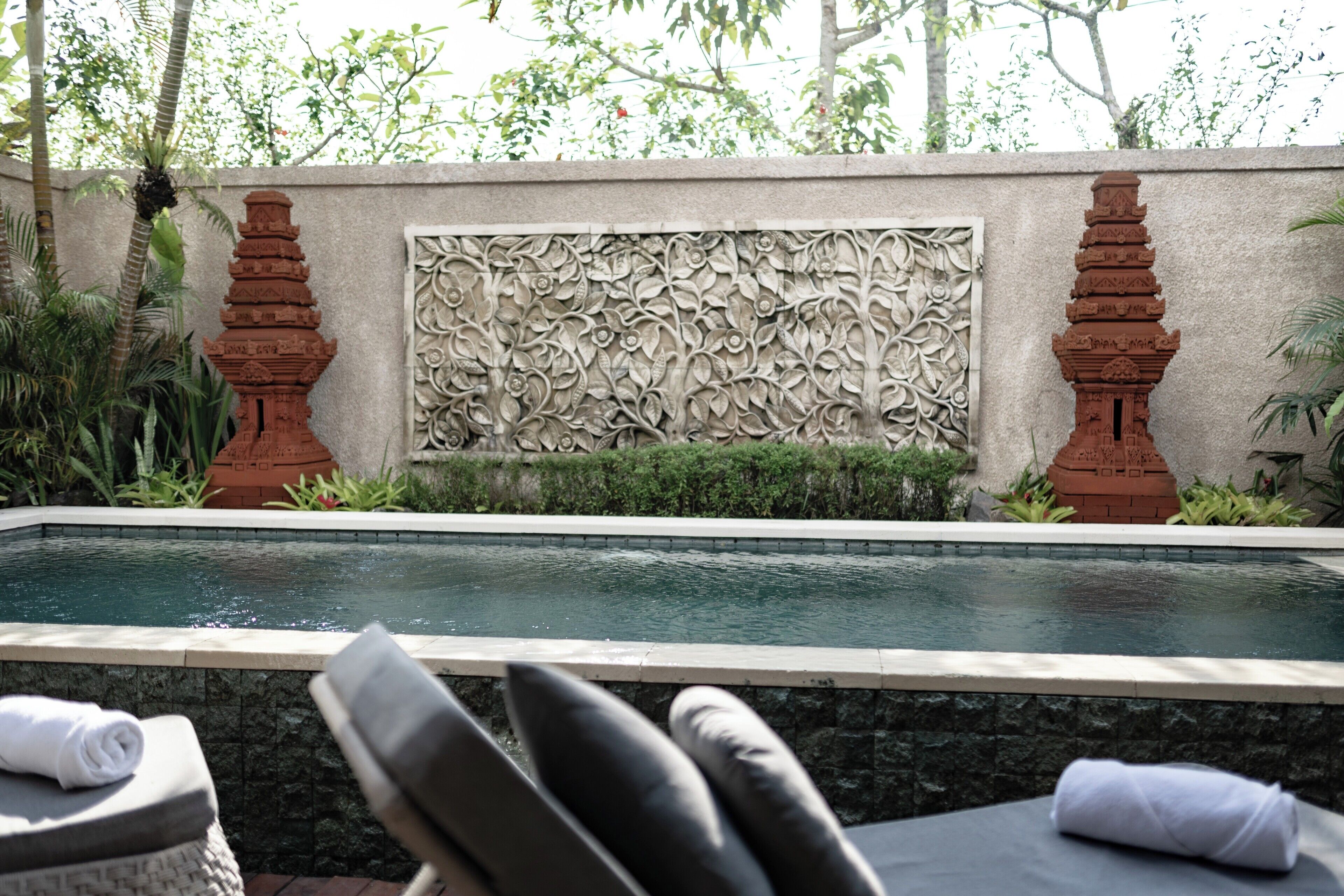 A pool area with a stone wall, two red pillars, and a lounge chair with a towel.