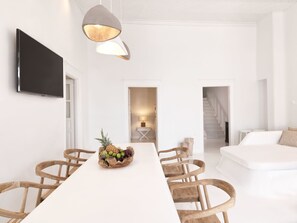 A modern, minimalist room with a long white table, wooden chairs, a fruit bowl, a flat-screen TV, and a staircase leading to another level. - Villa Kampani Sea View Villa in Mykonos Town (Mykonos)