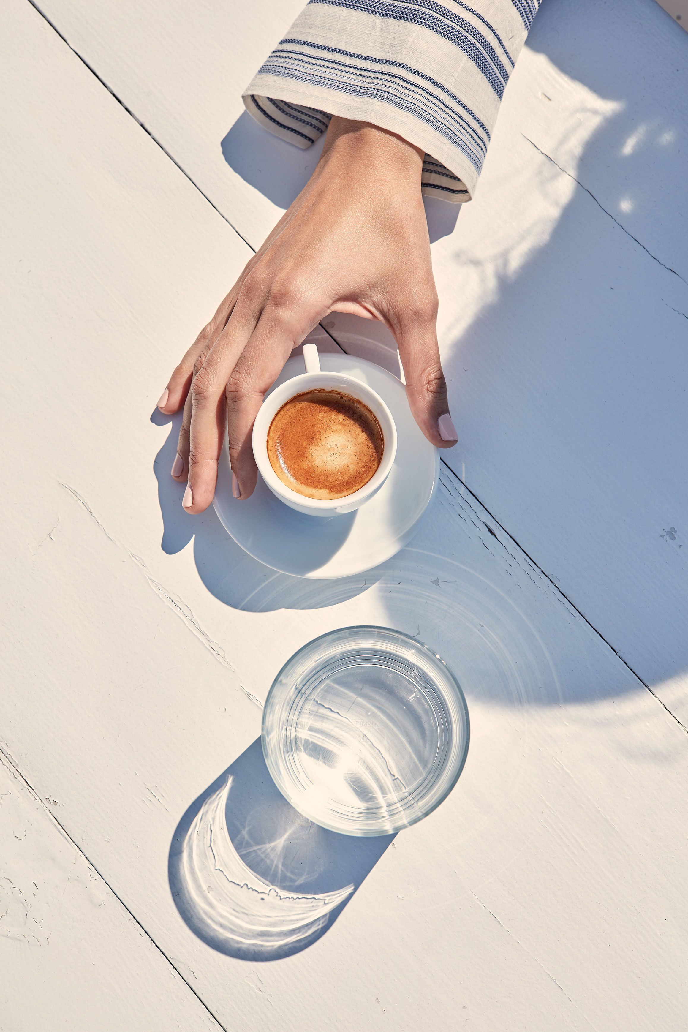 Eine Hand hält eine Kaffeetasse auf einem weißen Holztisch.