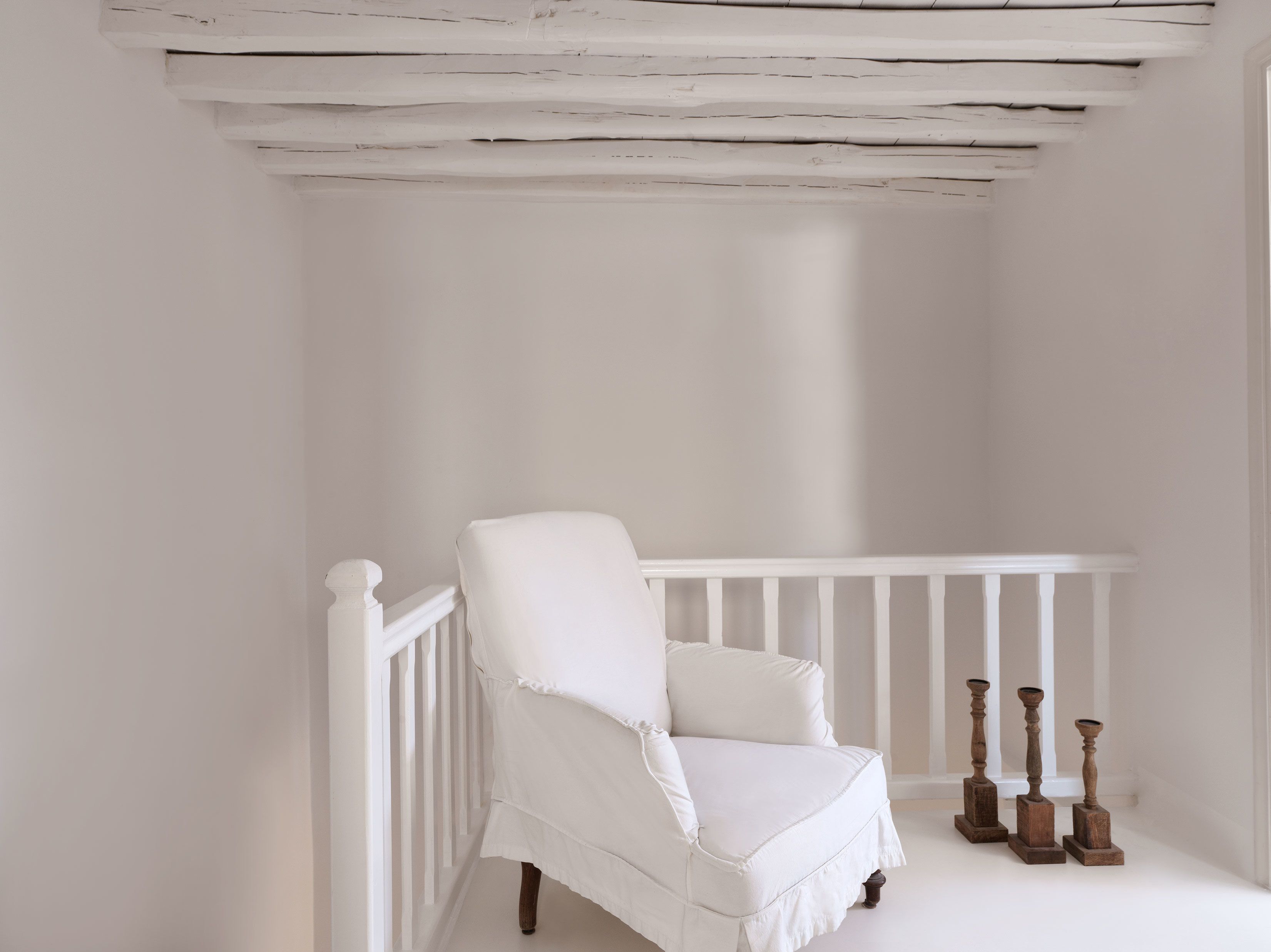 Uma cadeira branca com base de madeira e corrimão branco em um quarto com paredes brancas e teto de madeira.