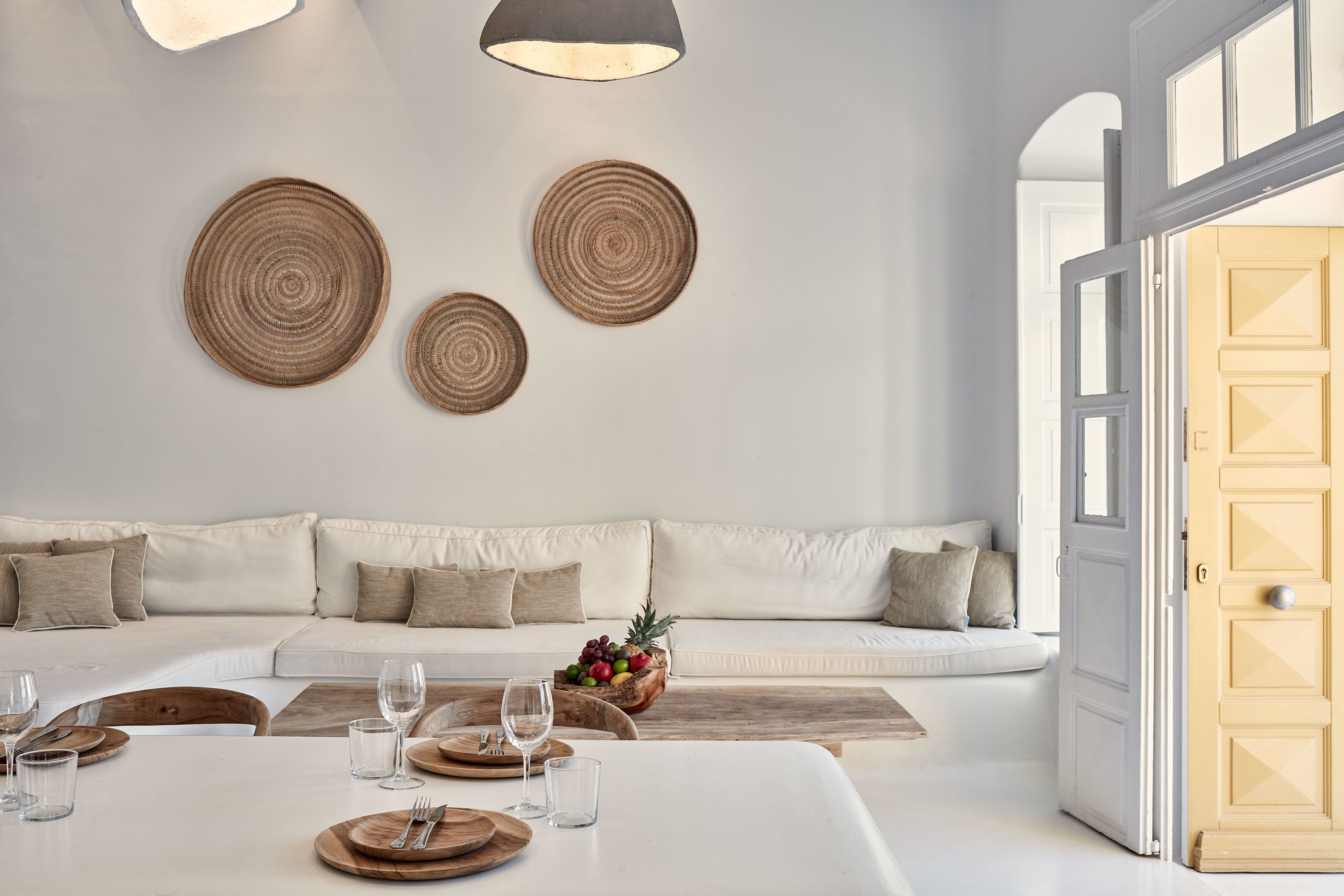 A modern living room with a white sofa, a dining table set with cutlery and glasses, and a fruit bowl on the coffee table.