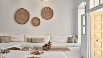 A modern living room with a white sofa, a dining table set with cutlery and glasses, and a fruit bowl on the coffee table.