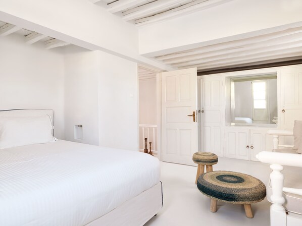 A white bedroom with a bed, a wooden chair, and a small stool.