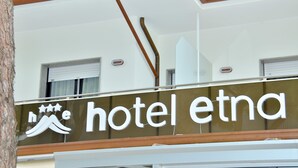 Ein Hotelschild mit der Aufschrift 'hotel etna' und einem Logo, das drei Sterne und eine Welle zeigt.