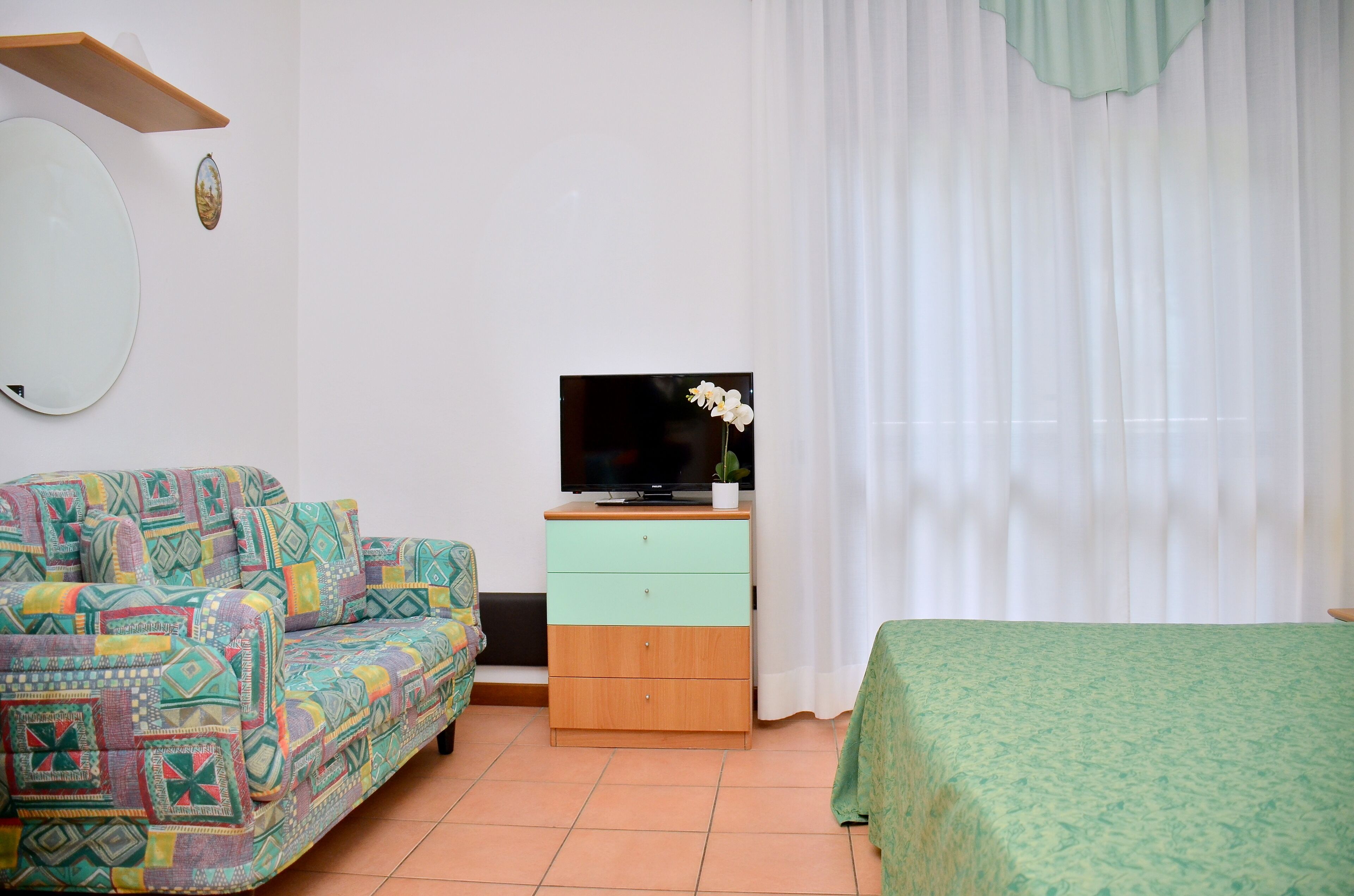 Una habitación con un sofá estampado, un pequeño mueble de madera con un televisor y una cama con colcha verde.