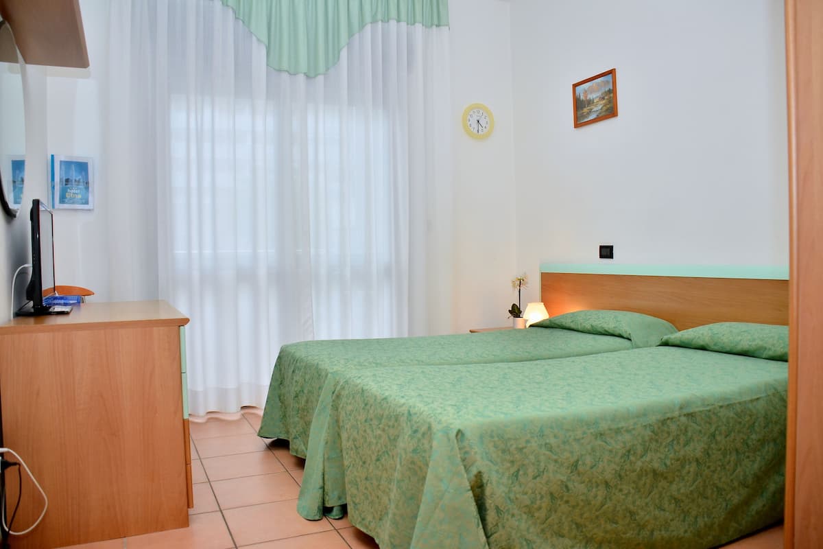 Ein Zimmer mit zwei Betten, einem Schreibtisch, einer Uhr und einem Bild an der Wand.