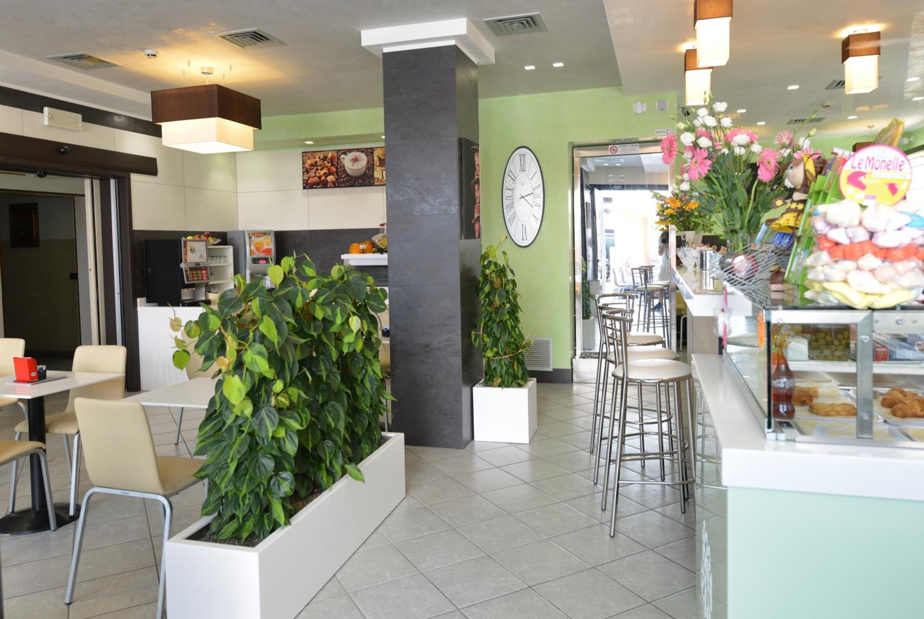 Ein modernes Café-Interieur mit Sitzgelegenheit, einer Theke mit Gebäck und einer Wanduhr.