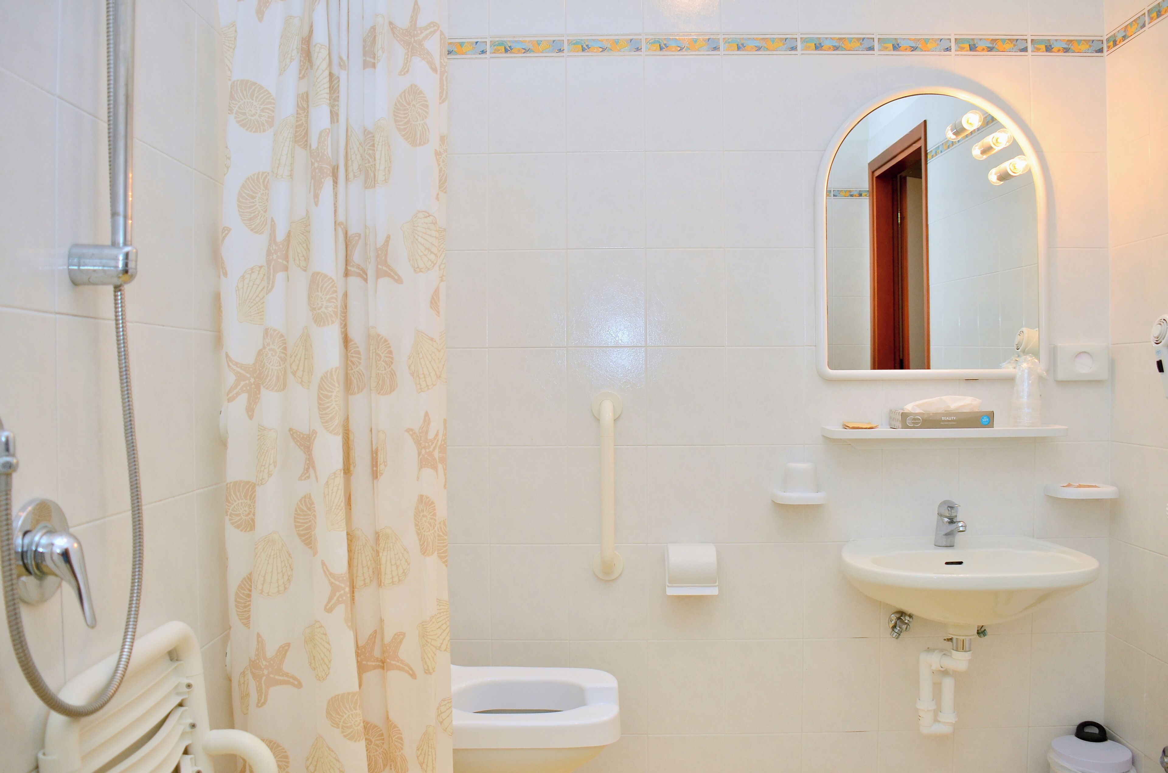 Un baño con inodoro, lavabo y ducha. Hay un espejo sobre el lavabo y una cortina de ducha con motivos de hojas.