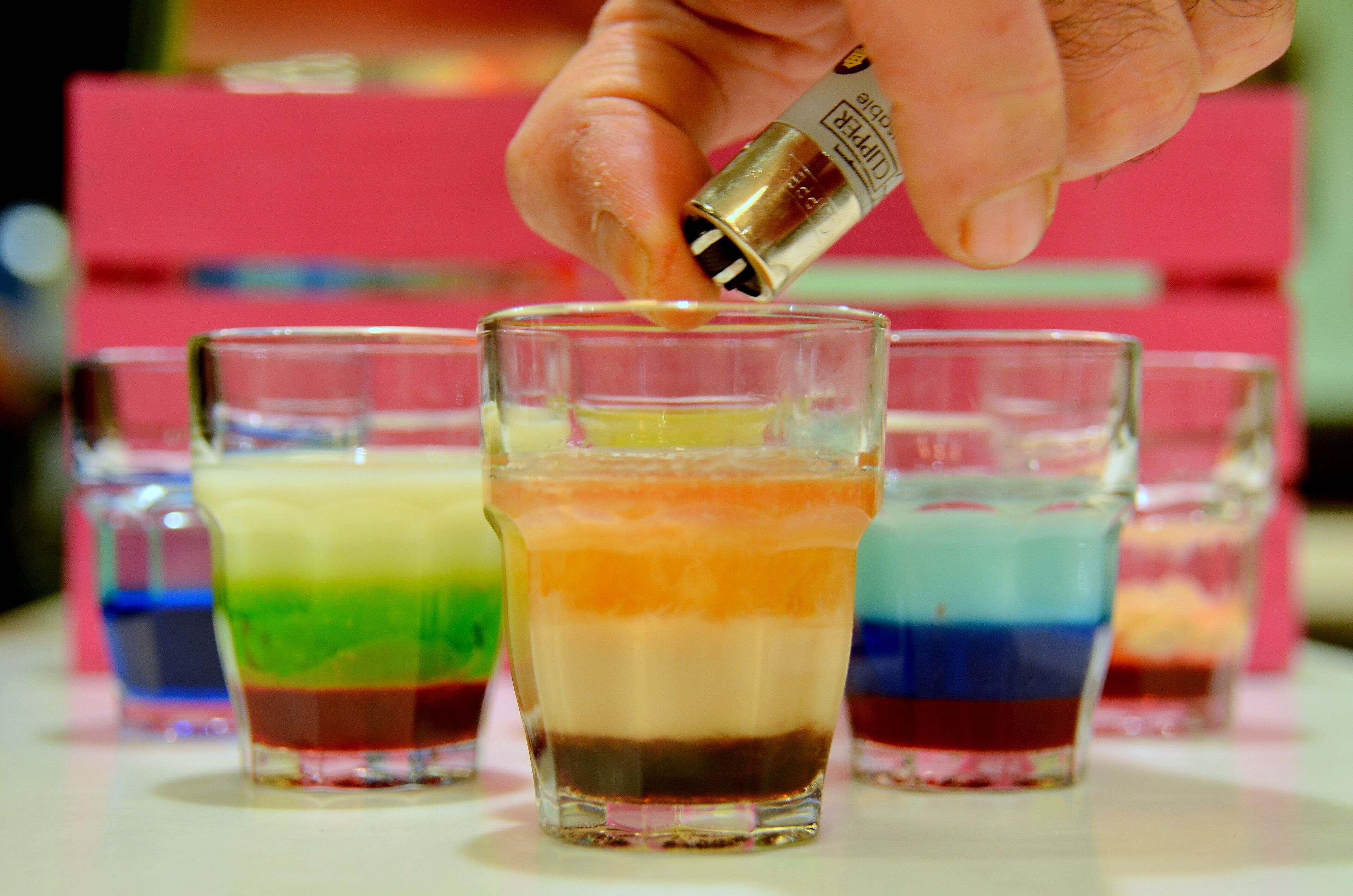 Una mano vertiendo un líquido dorado en un vaso con colores en capas.