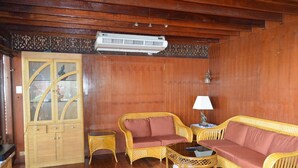 Habitació amb sòl de fusta, un seient de sofà, una taula petita amb una làmpada i un moble amb portes de vidre.