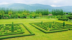 Un jardin bien entretenu, agrémenté de labyrinthes végétaux aux formes géométriques et d’un lac en arrière-plan.