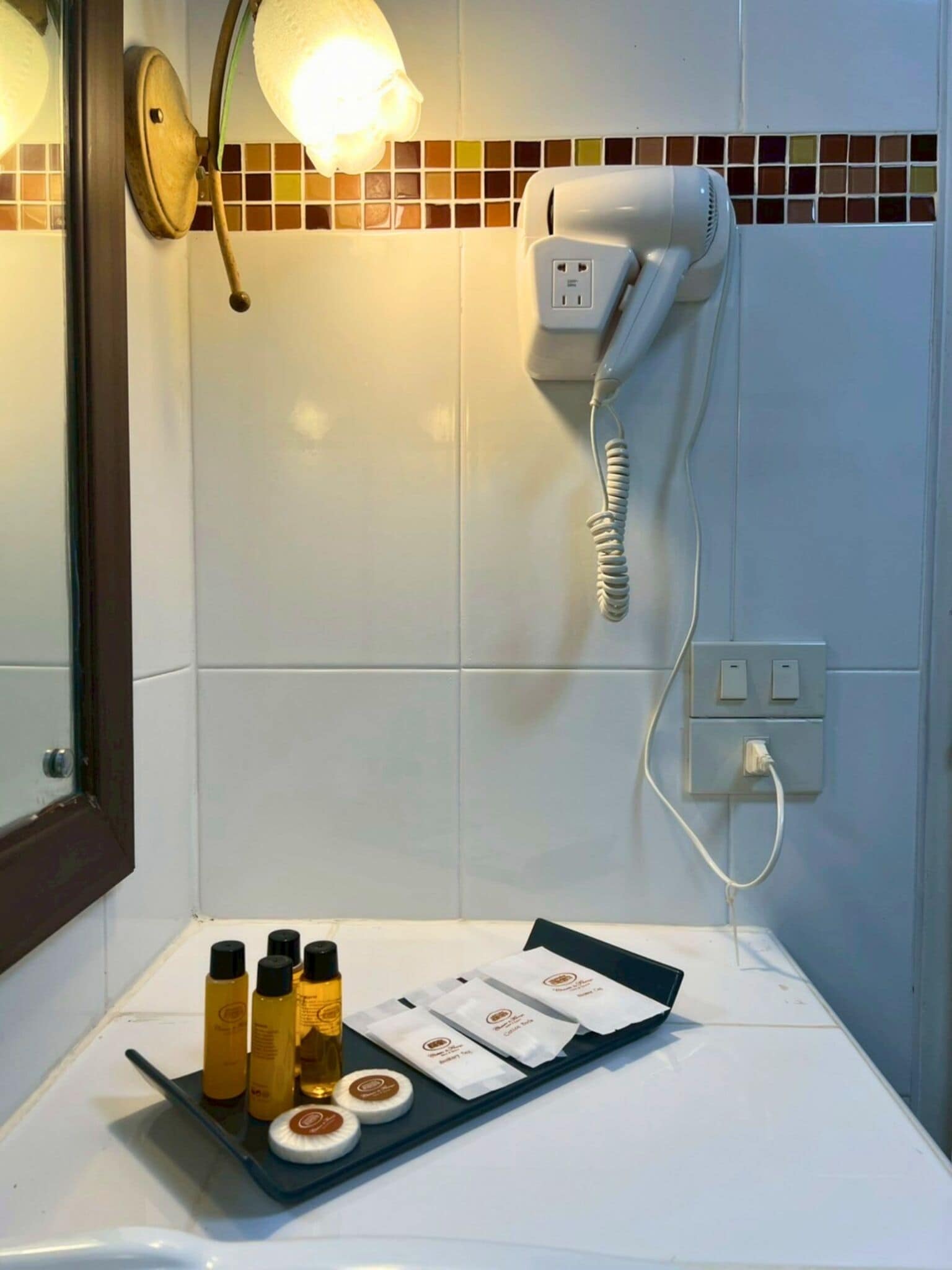 Un baño con secador de pelo, espejo y artículos de aseo en la encimera.
