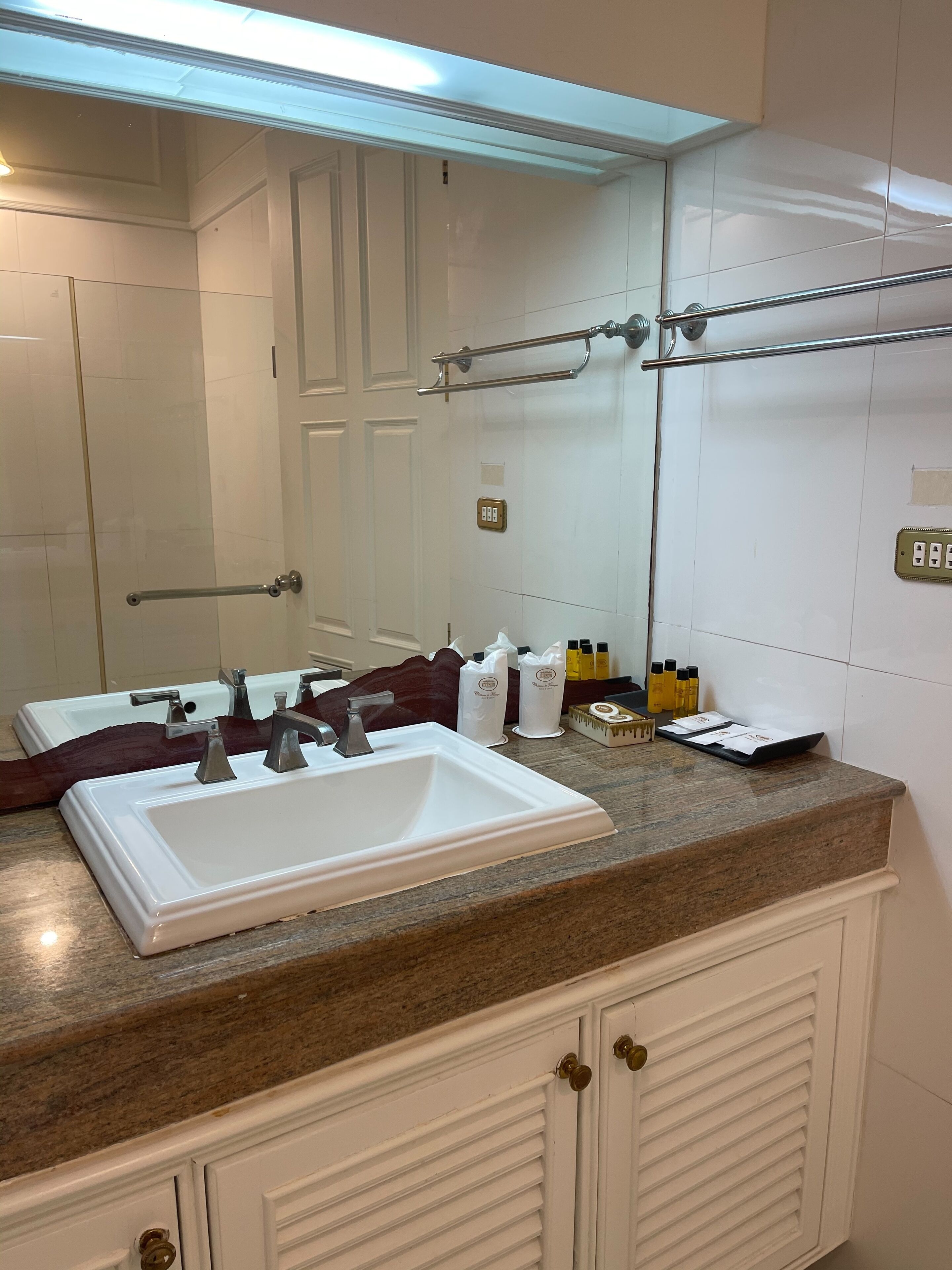 A bathroom with a white sink, two faucets, a mirror, and a towel rack.
