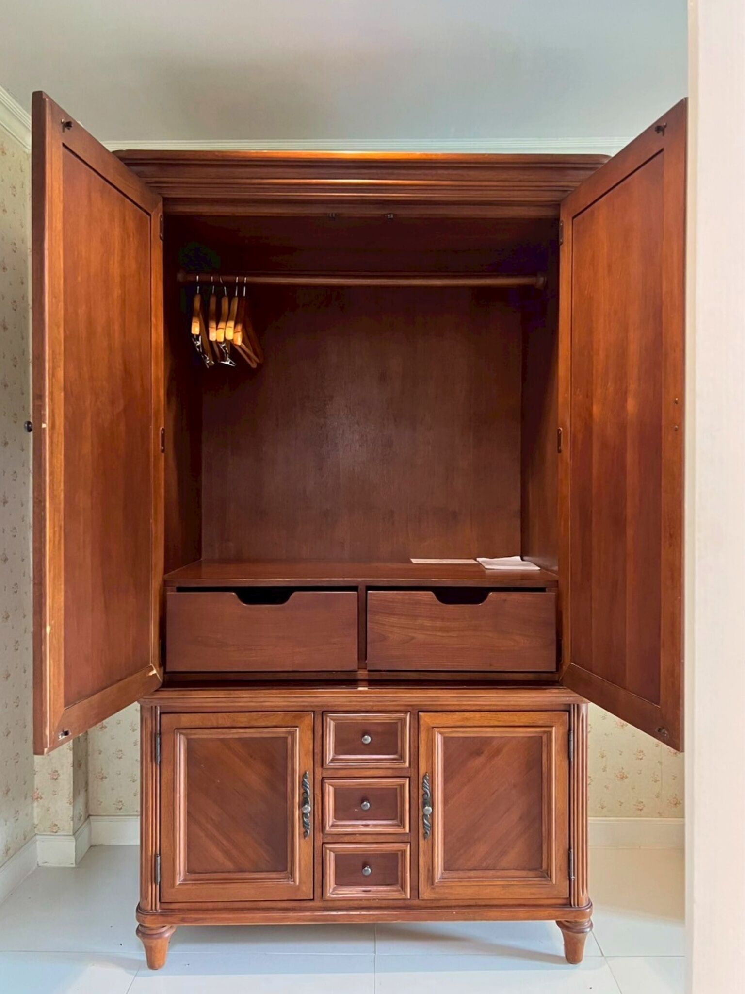 A wooden wardrobe with open doors, revealing a hanging rod and multiple drawers.