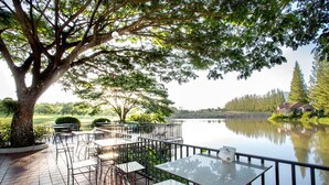 Une terrasse extérieure avec des tables et des chaises, donnant sur un lac paisible et entourée d’arbres.