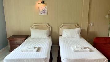 A hotel room with two single beds, a nightstand, a red chair, and a wall-mounted light fixture.