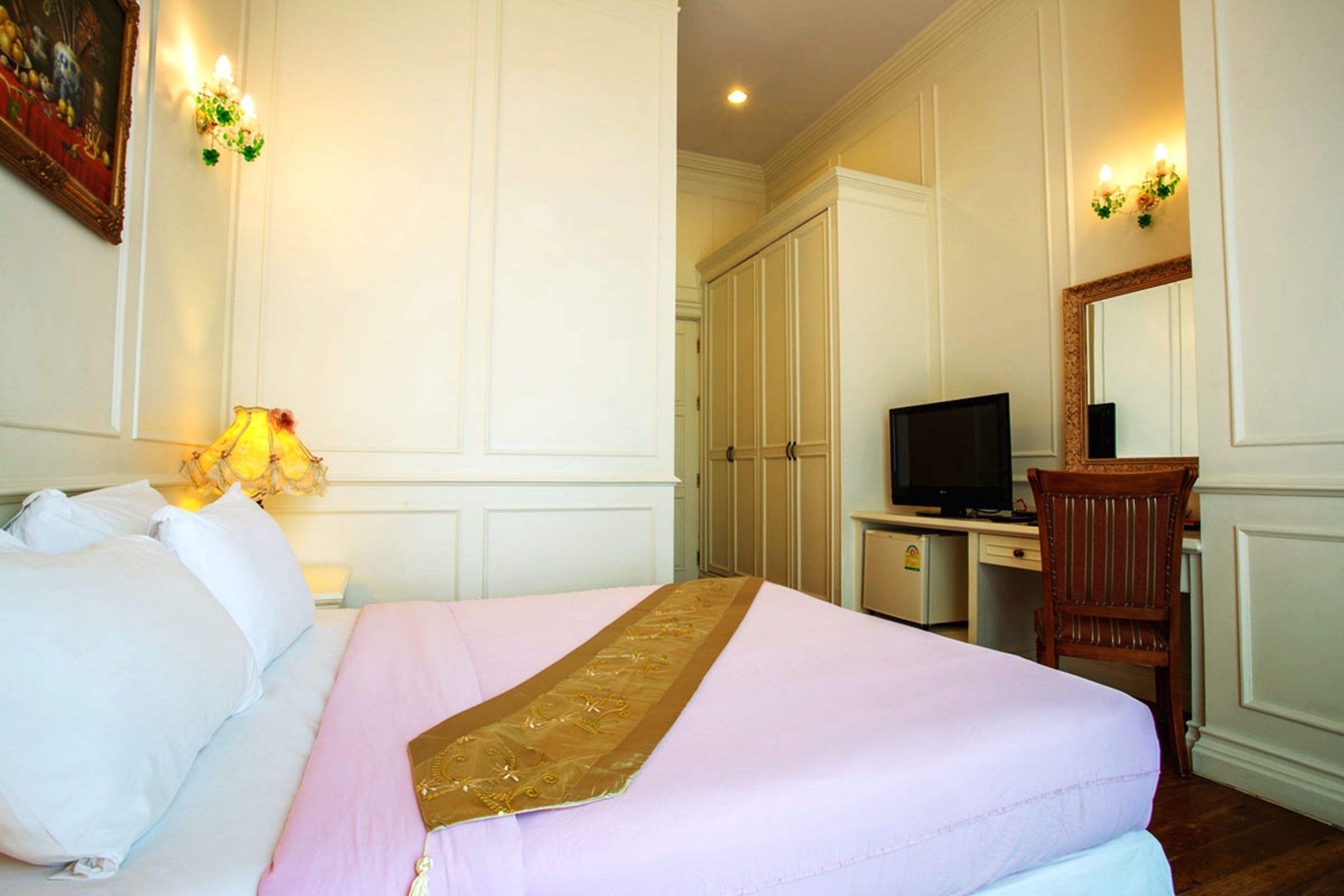 A hotel room with a bed, a desk with a television, a chair, and a wardrobe.