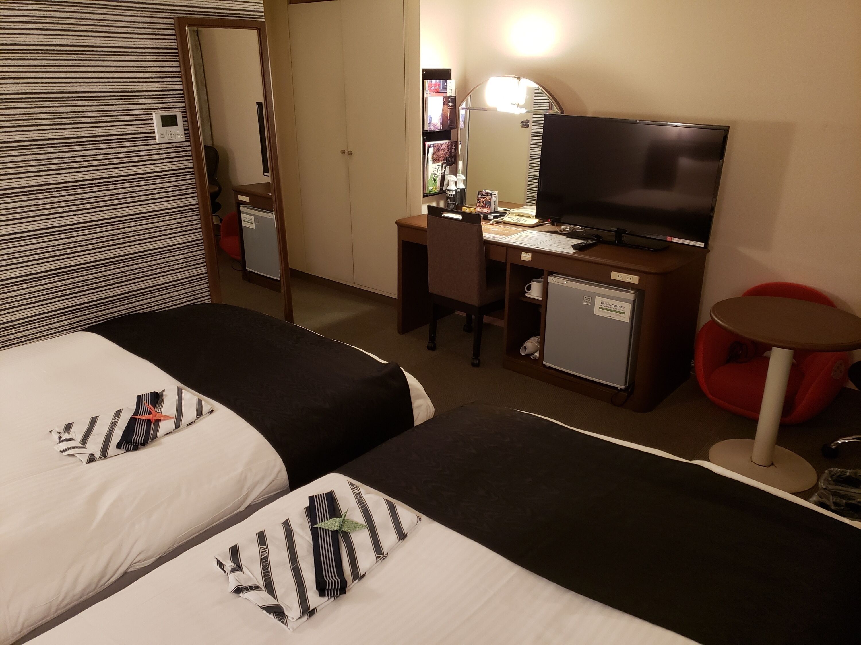 A hotel room with two beds, a desk with a computer, a television, and a small refrigerator.
