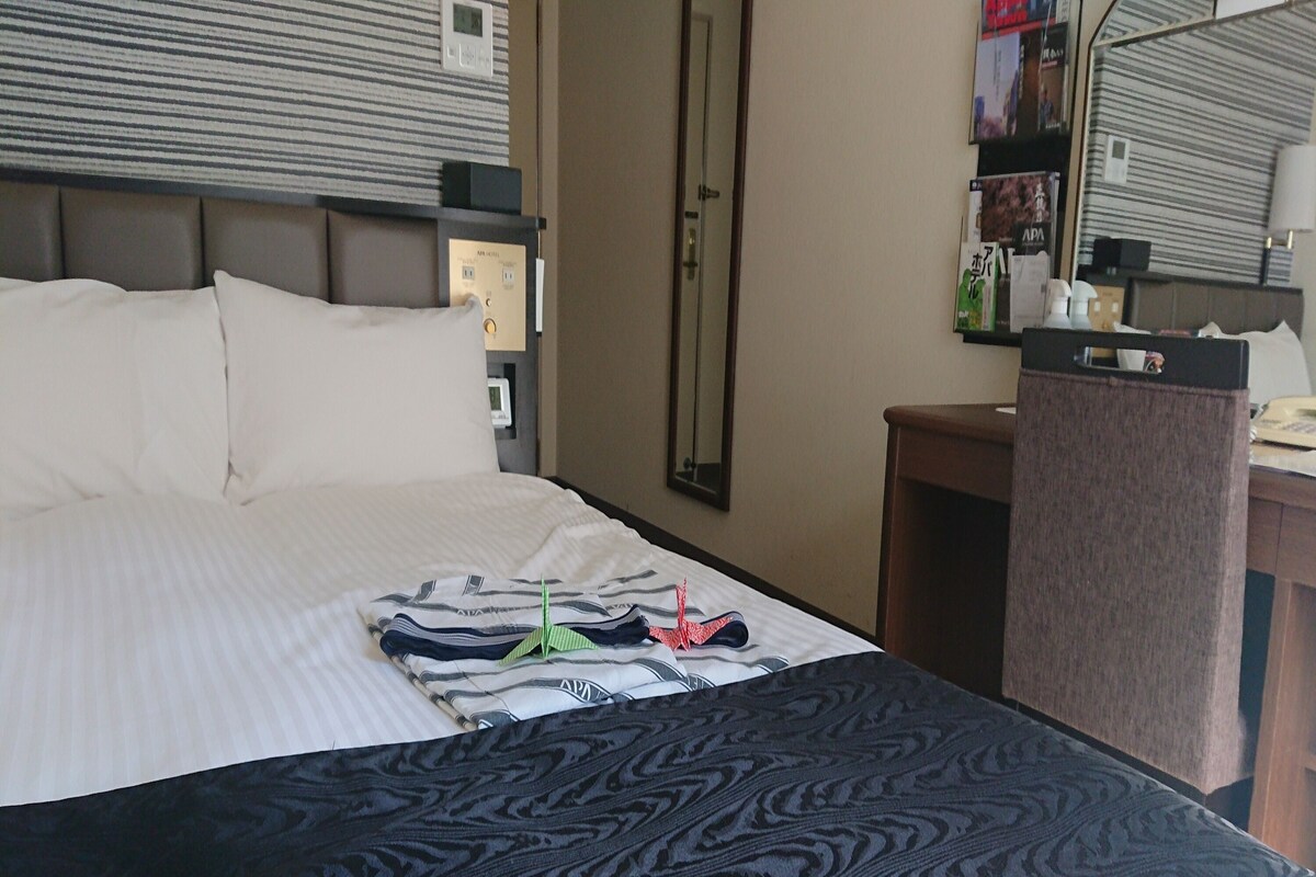 A hotel room with a bed, a desk, and a mirror.