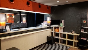 A hotel reception area with a counter, a reception desk, a TV, and a shelf with magazines. - APA Hotel Owariichinomiya Station (Ichinomiya)