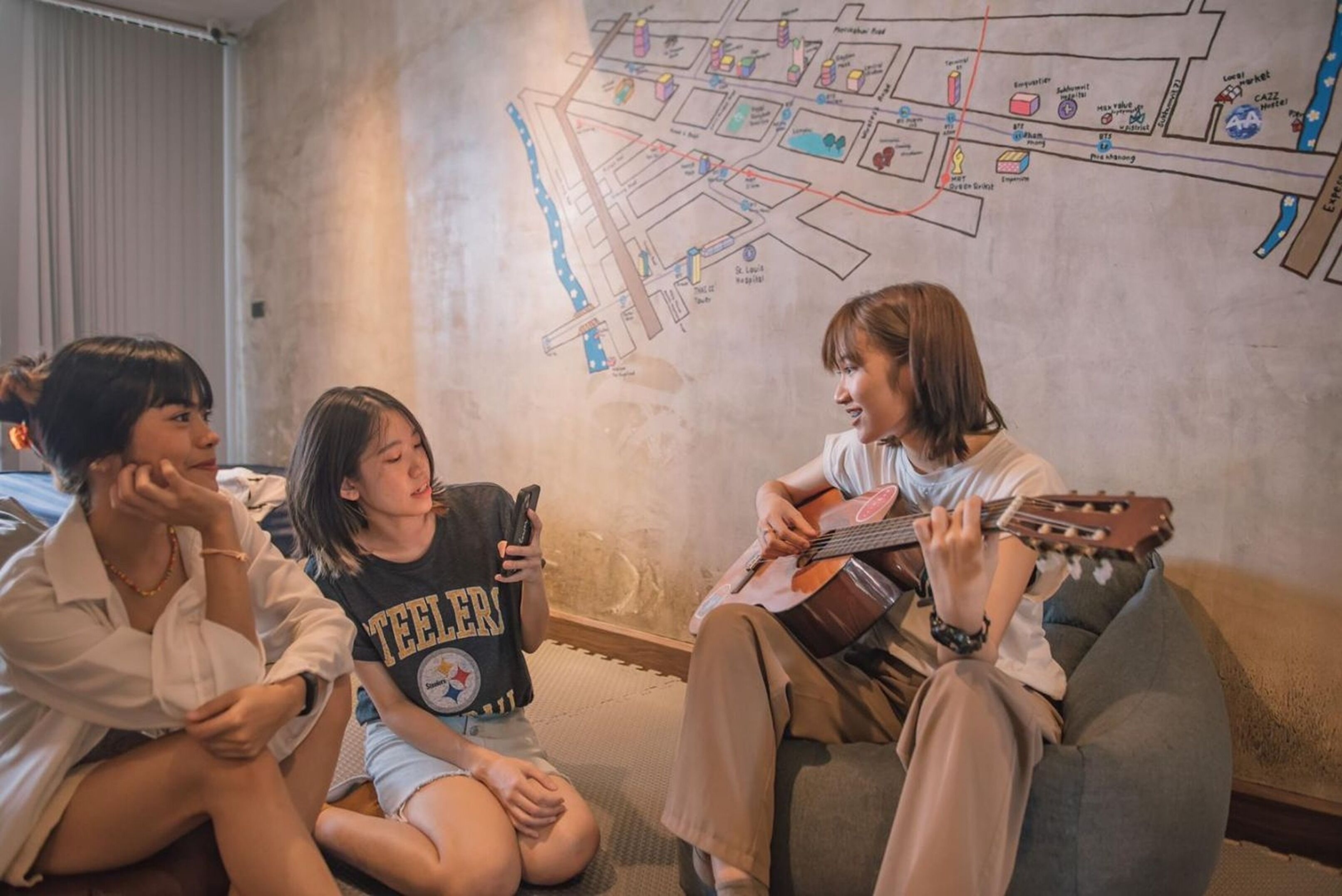 Three people sitting on a bean bag in a room with a map on the wall.