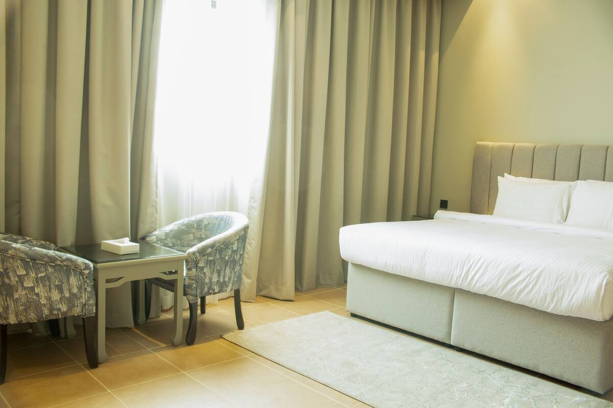 A hotel room with a bed, a desk, two chairs, and a window with curtains.