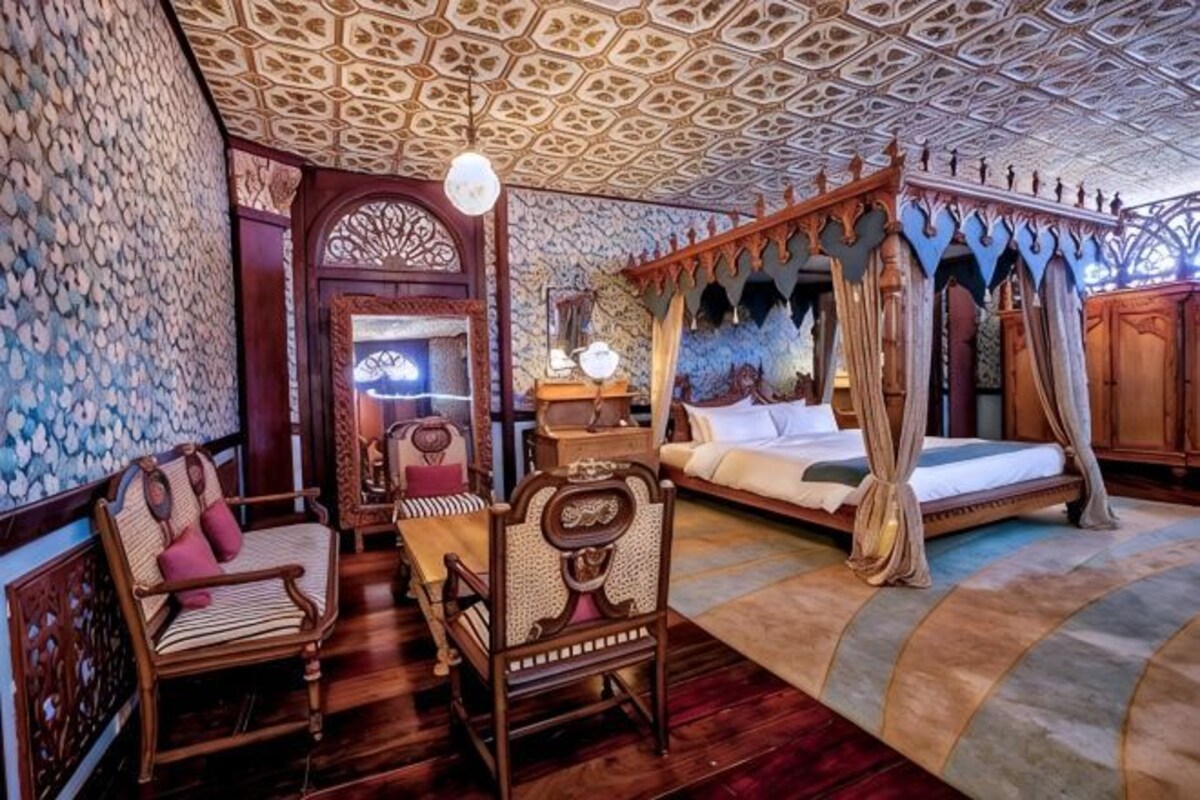 Une chambre de style traditionnel, dotée d’un lit à baldaquin, d’un coin salon avec des fauteuils et d’un plafond orné de motifs.