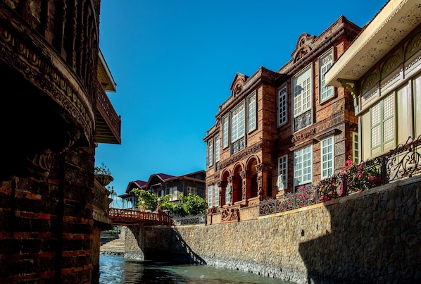 A historic building with intricate brickwork and large windows, a stone bridge, and a canal.